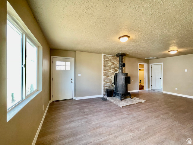 255 West Main Street Mount Pleasant, UT 84647 - Photo 14 of 35 Spacious room featuring wood-finish flooring, a prominent wood-burning stove with a brick hearth, and a decorative stone accent wall