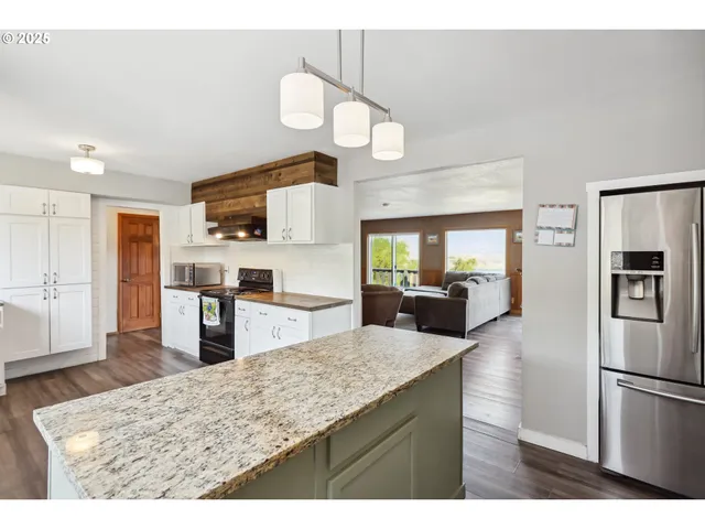 a kitchen with stainless steel appliances kitchen island granite countertop a refrigerator a stove and a sink with wooden floor