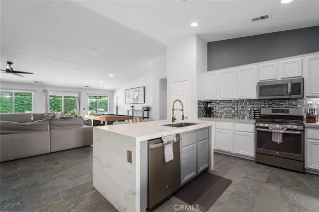 a kitchen with stainless steel appliances granite countertop a stove top oven a sink a refrigerator white cabinets and couches with wooden floor