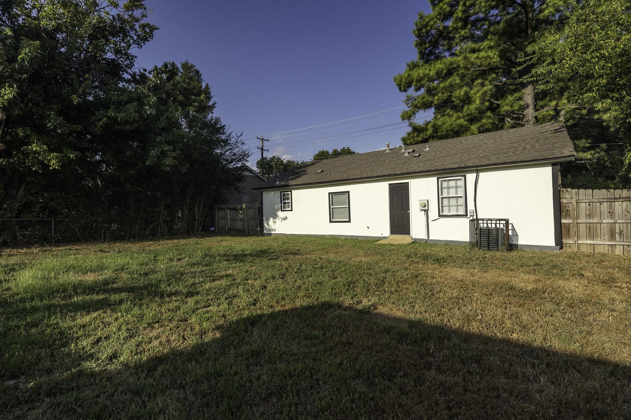 4780 Hillbrook Road Memphis, TN 38109 - Photo 5 of 25 Expansive grassy yard with a wood fence boundary, featuring a white exterior structure with dark trim windows and a dark entry door