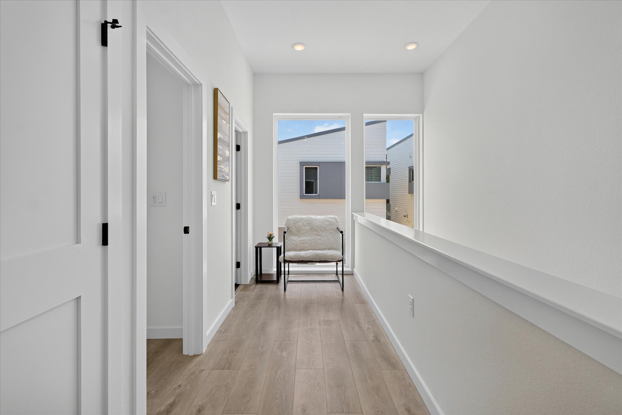 2000 Riverside Farms Road, Unit 8101 Austin, TX 78741 - Photo 14 of 41 This photo shows a bright, modern hallway with light wood flooring and white walls. It features recessed lighting, two large windows providing natural light, and a cozy seating area with a side table. The space is simple and inviting.