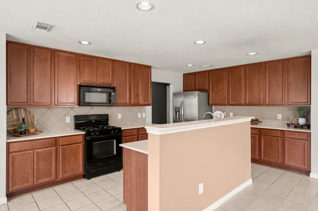 a kitchen with stainless steel appliances granite countertop a stove top oven a sink dishwasher and a refrigerator with wooden cabinets