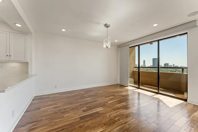 a view of an empty room and kitchen with wooden floor