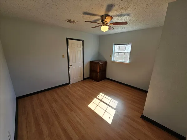 an empty room with wooden floor chandelier fan and windows