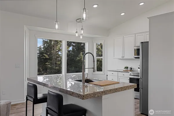 a kitchen with stainless steel appliances kitchen island granite countertop a refrigerator a stove oven and white cabinets with wooden floors