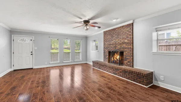 a view of an empty room with wooden floor fireplace and a window