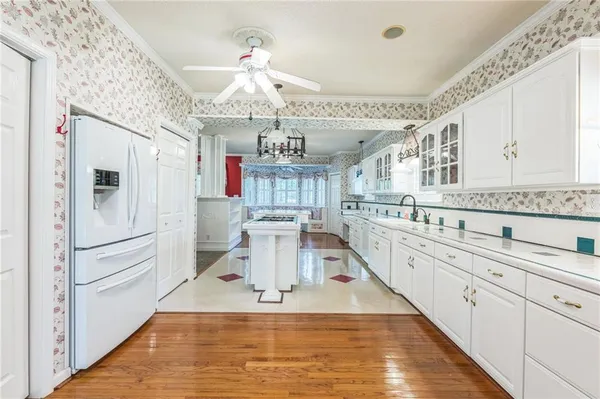 a large white kitchen with kitchen island a stove a sink dishwasher and white cabinets with wooden floor
