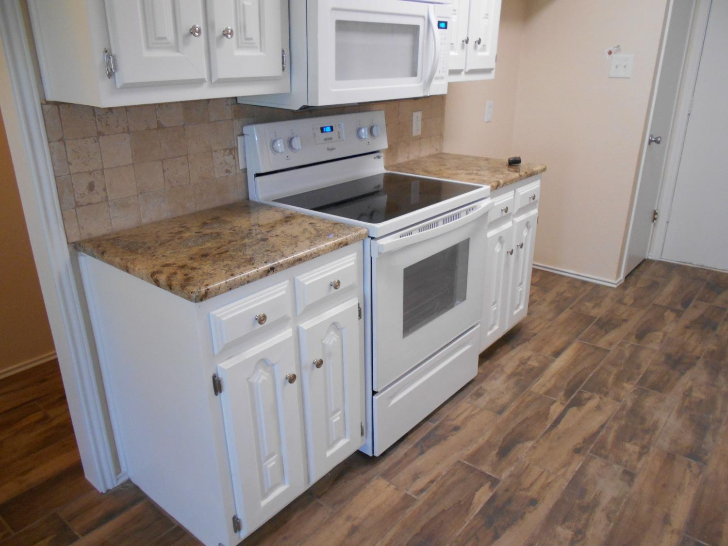 5739 Emory Street Lubbock, TX 79416 - Photo 7 of 14 a kitchen with granite countertop white cabinets and white appliances