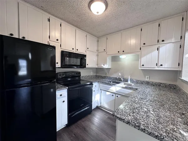 a kitchen with granite countertop a refrigerator stove and white cabinets