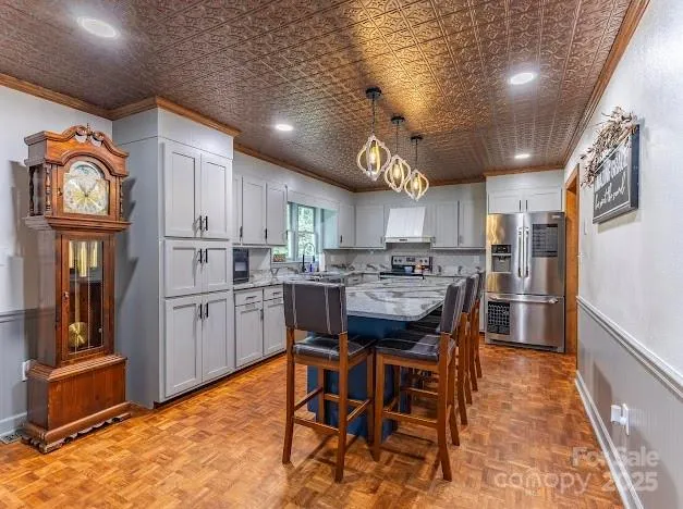 a kitchen with stainless steel appliances kitchen island granite countertop a refrigerator a stove a sink a dining table and chairs with wooden floor