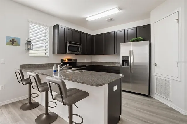 a kitchen with stainless steel appliances granite countertop a refrigerator a stove a sink and a microwave with wooden floor