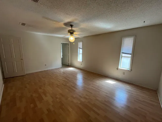 an empty room with wooden floor chandelier fan and windows