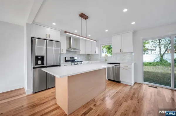 a kitchen with stainless steel appliances granite countertop a refrigerator a sink dishwasher a s stove top oven a large island with wooden floor and cabinets