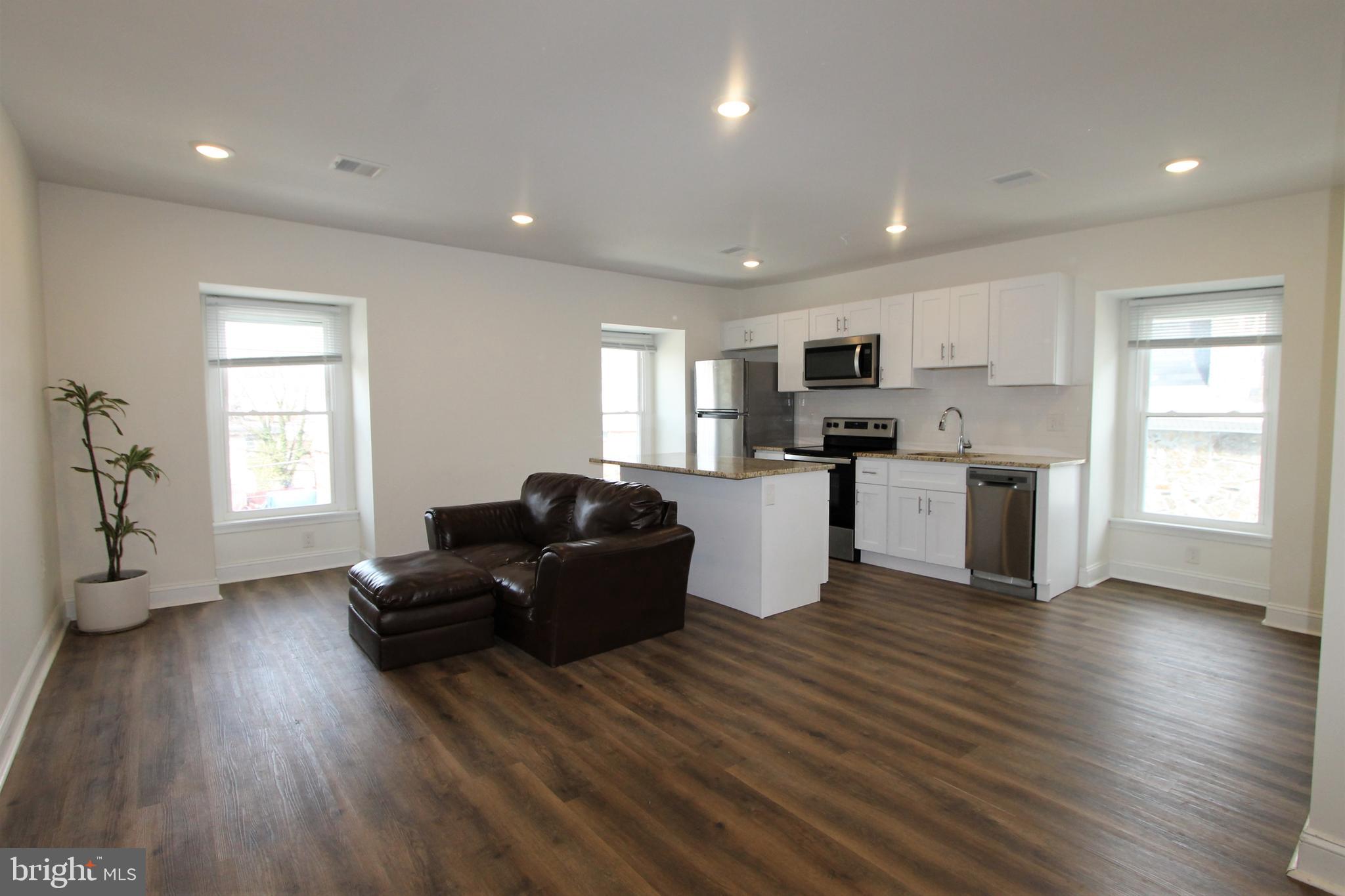 a living room with stainless steel appliances kitchen island granite countertop wooden floors and a window