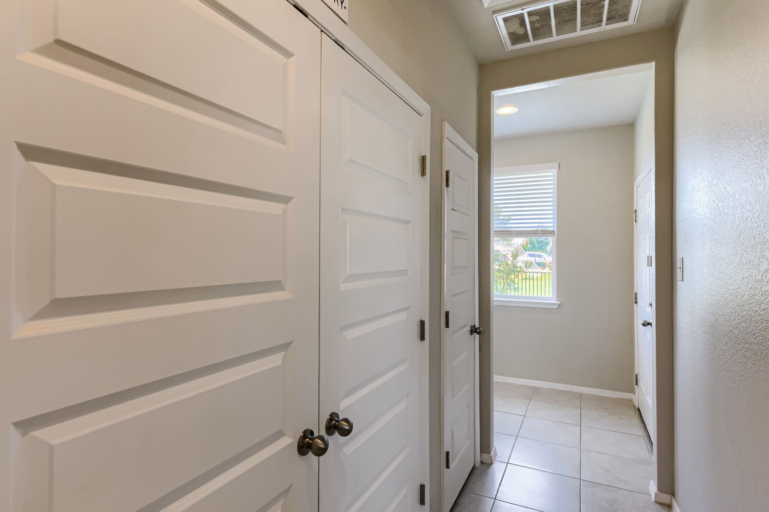 1310 Goforth Road Kyle, TX 78640 - Photo 5 of 24 Hallway featuring multiple paneled doors, neutral wall paint, tile flooring, and a window with blinds