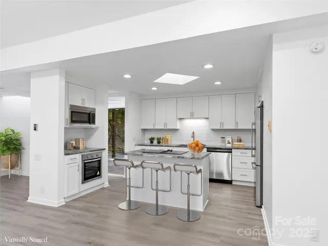 a kitchen with stainless steel appliances a stove a sink a refrigerator white cabinets and wooden floor