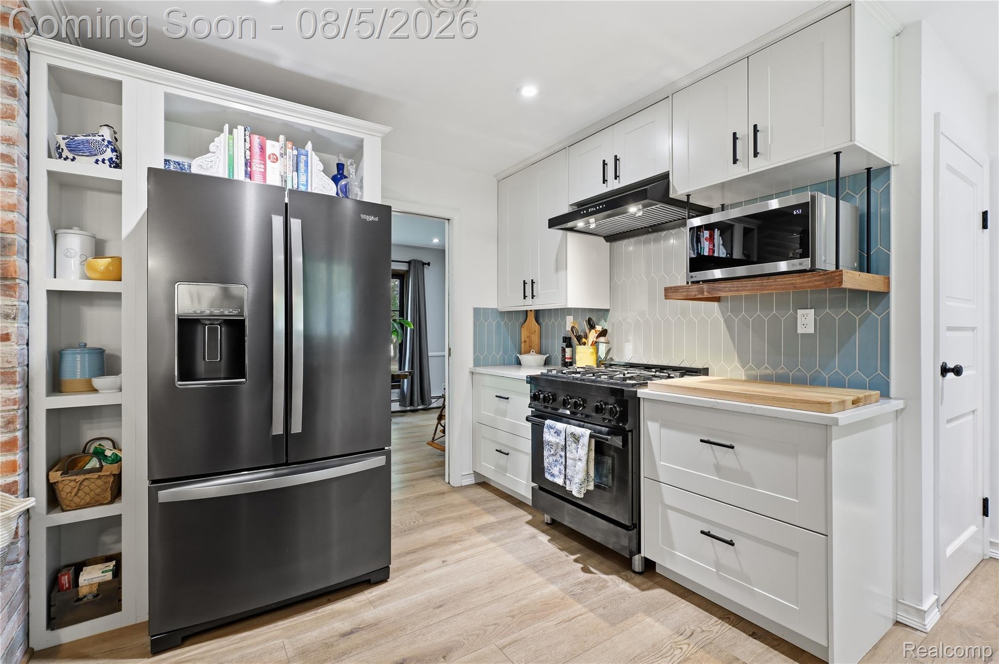 6478 West Stanley Road Mount Morris, MI 48458 - Photo 34 of 80 Modern kitchen featuring stainless steel appliances, light wood-finish flooring, white cabinetry with black hardware, a blue geometric tile backsplash, and built-in shelving