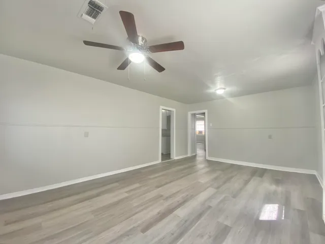 an empty room with wooden floor fan and windows
