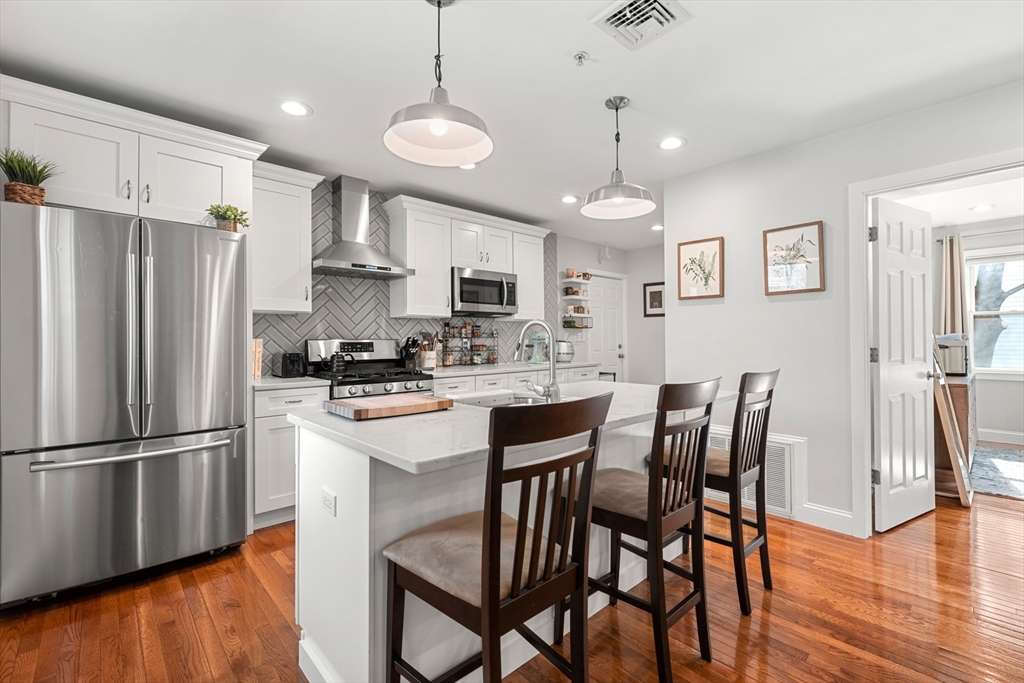 a kitchen with stainless steel appliances granite countertop a dining table chairs refrigerator and cabinets