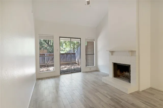an empty room with wooden floor fireplace and windows