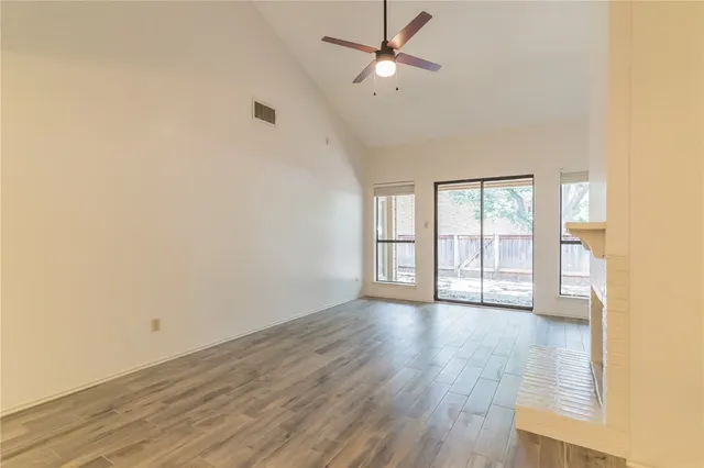 an empty room with wooden floor fan and windows