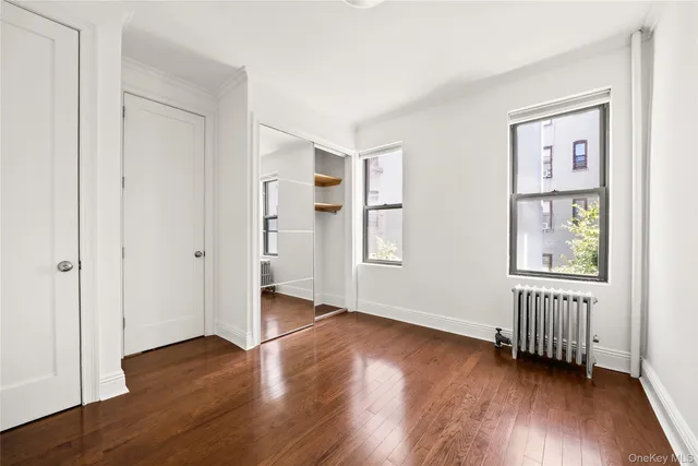 an empty room with wooden floor closet and windows