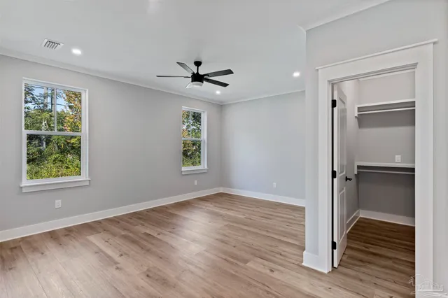 a view of an empty room with wooden floor ceiling fan and a window