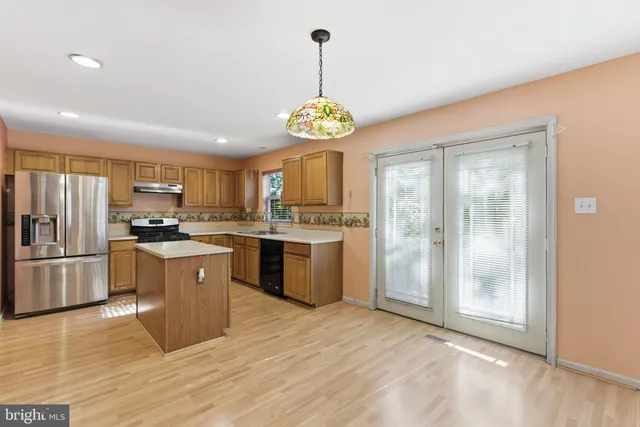 a kitchen with stainless steel appliances granite countertop a refrigerator a sink dishwasher a stove and a dining table with wooden floor