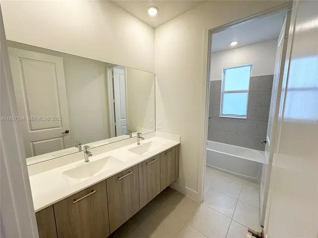 a bathroom with a double vanity sink and mirror with bathtub
