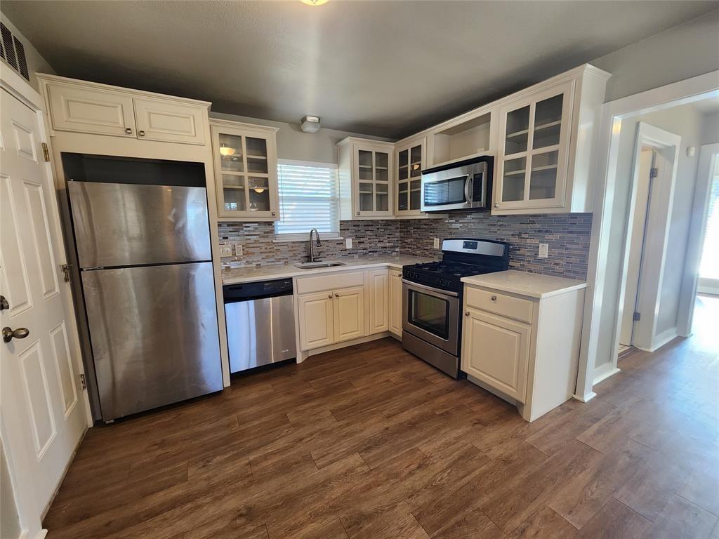 Kitchen featuring stainless steel appliances, glass insert cabinets, dark wood-type flooring, white cabinets, and decorative backsplash