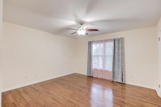 an empty room with wooden floor chandelier fan and windows