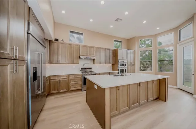 a large kitchen with kitchen island a large window a sink stainless steel appliances and a window