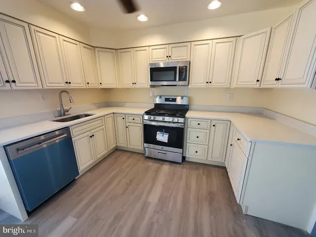 a kitchen with stainless steel appliances granite countertop white cabinets a sink a stove a microwave and wooden floors