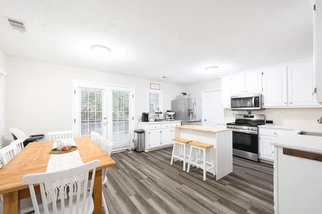 a open kitchen with stainless steel appliances granite countertop a stove top oven a sink dishwasher a dining table and chairs with wooden floor