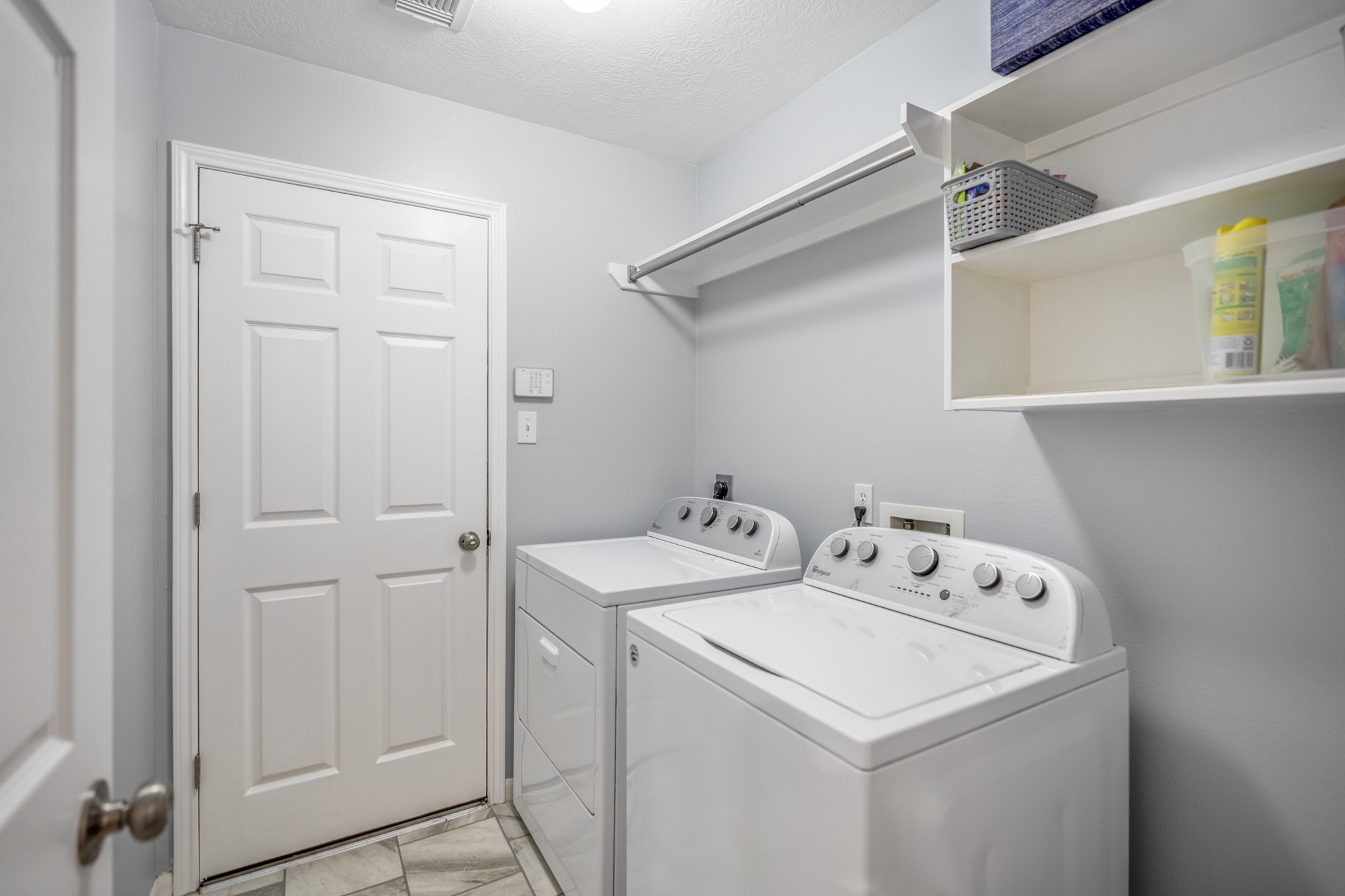 3411 Utah Beach Court Spring, TX 77388 - Photo 33 of 50 Utility room placement keeps daily routines tucked neatly off the hallway, with built-in cabinetry and shelving above the washer and dryer for added storage. The door ahead connects directly to the garage, making this a practical drop zone between the garage entry, secondary bedroom hall, and main living areas.