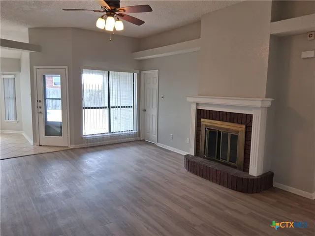 a view of an empty room with wooden floor fireplace and a window