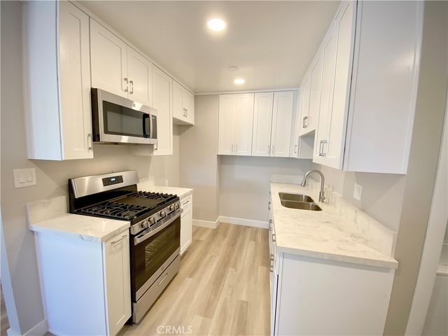 a kitchen with granite countertop a sink a stove top oven and cabinetry