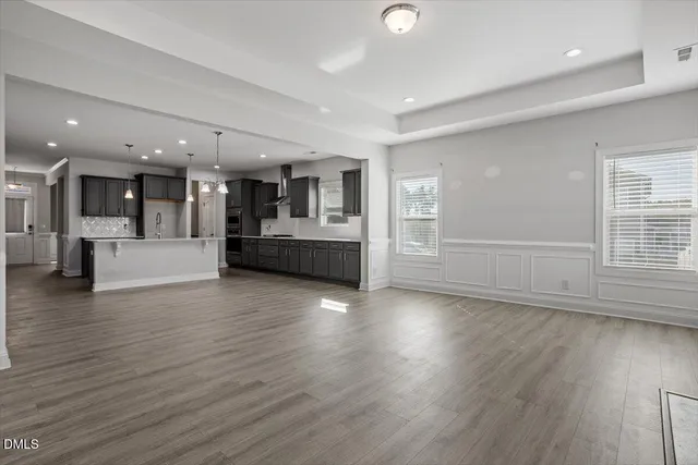 an empty room with wooden floor and kitchen view