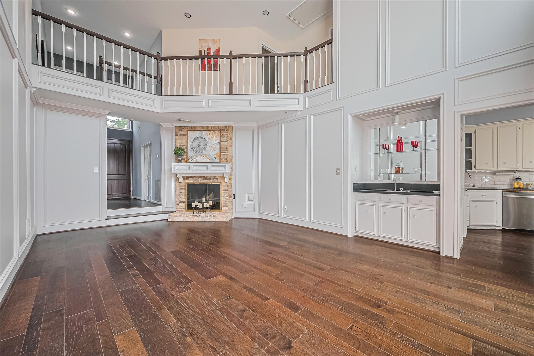 4305 Westheimer Road Houston, TX 77027 - Photo 4 of 25 Stunning two-story living area featuring rich hardwood floors, a cozy brick fireplace, and a stylish wet bar, seamlessly opening to a modern kitchen.