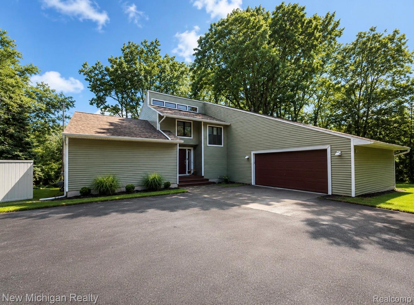 7156 East River Road Flushing, MI 48433 - Photo 1 of 35 Contemporary home exterior with sage green siding and a striking brown garage door