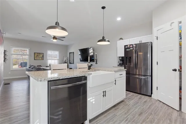 a kitchen with stainless steel appliances granite countertop a refrigerator a sink dishwasher a stove and a dining table with wooden floor