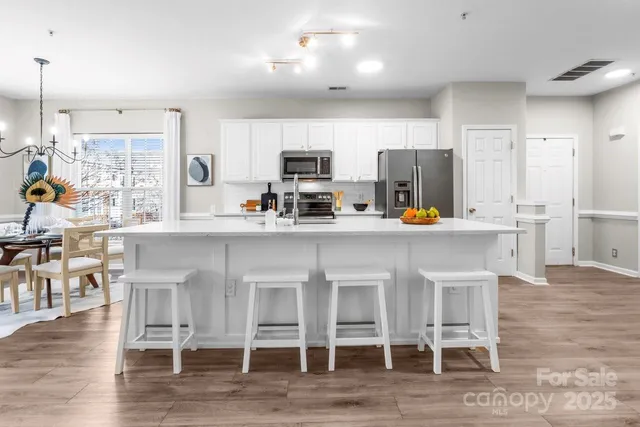 a kitchen with stainless steel appliances a dining table chairs refrigerator and sink