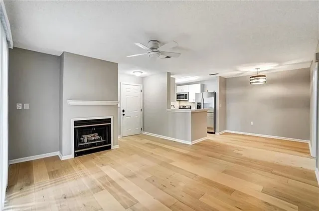 a view of a livingroom with a fireplace a ceiling fan and wooden floor