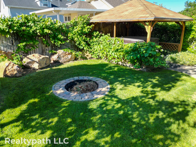 475 South 300 East Payson, UT 84651 - Photo 9 of 12 Manicured backyard featuring a stone fire pit, a wooden gazebo with a shingle roof, and a privacy fence lined with mature foliage