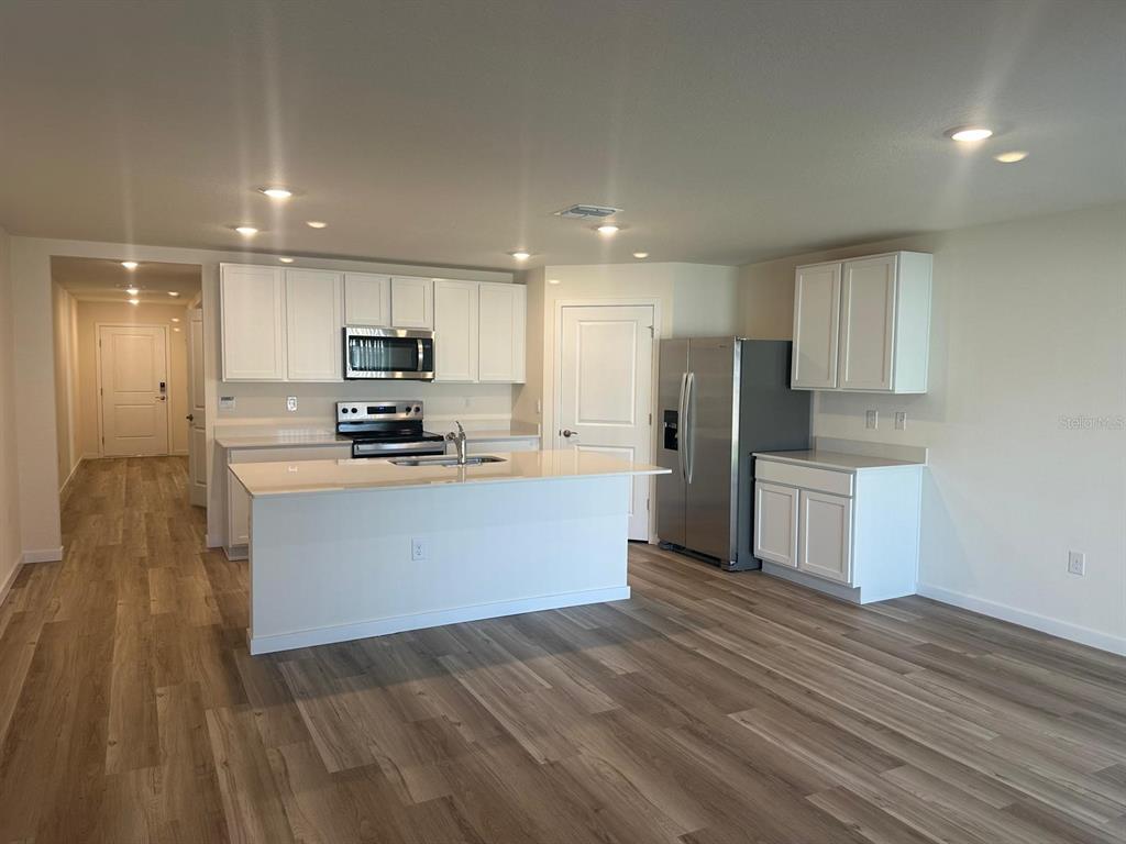 4697 Southwest 89th Street Ocala, FL 34476 - Photo 2 of 11 a large kitchen with kitchen island a sink dishwasher a refrigerator and white cabinets with wooden floor