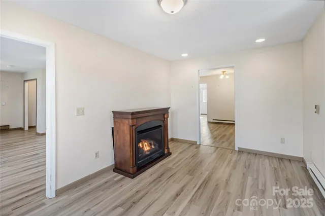 a view of an empty room with wooden floor fireplace and a window