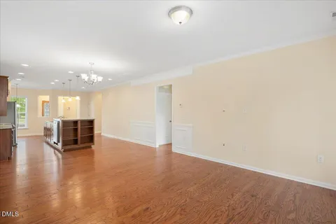 an empty room with wooden floor and a kitchen