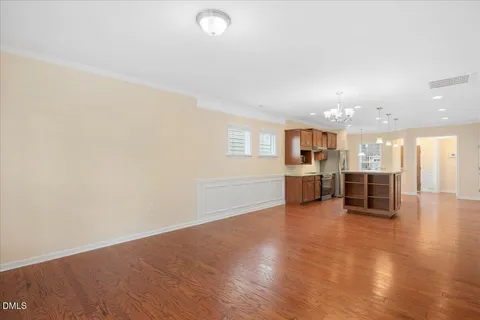 an empty room with wooden floor and kitchen view