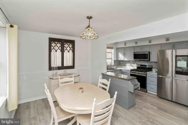 a kitchen with stainless steel appliances a stove a sink dishwasher a refrigerator and a dining table with wooden floor