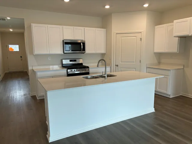 a kitchen with stainless steel appliances granite countertop a sink a stove a microwave a refrigerator a white cabinets and wooden floor